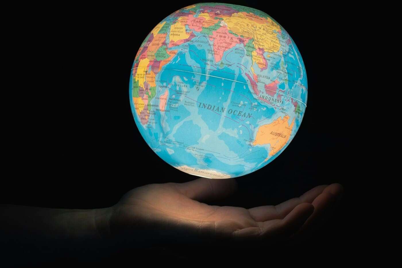 Globo terráqueo iluminado sobre mano humana, representando globalización y filosofía.