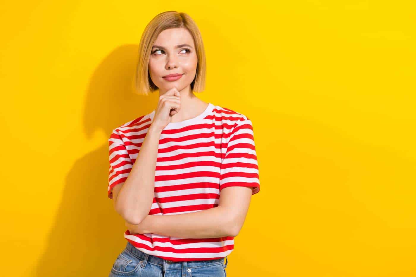 Pensativa mujer joven en camiseta a rayas en fondo amarillo brillante.