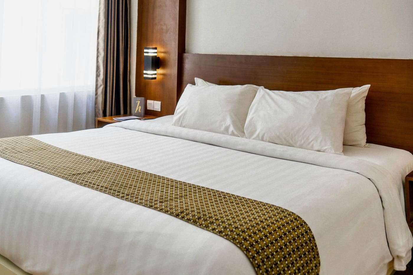 Habitación de hotel moderna con cama grande, ropa blanca y detalles decorativos elegantes.