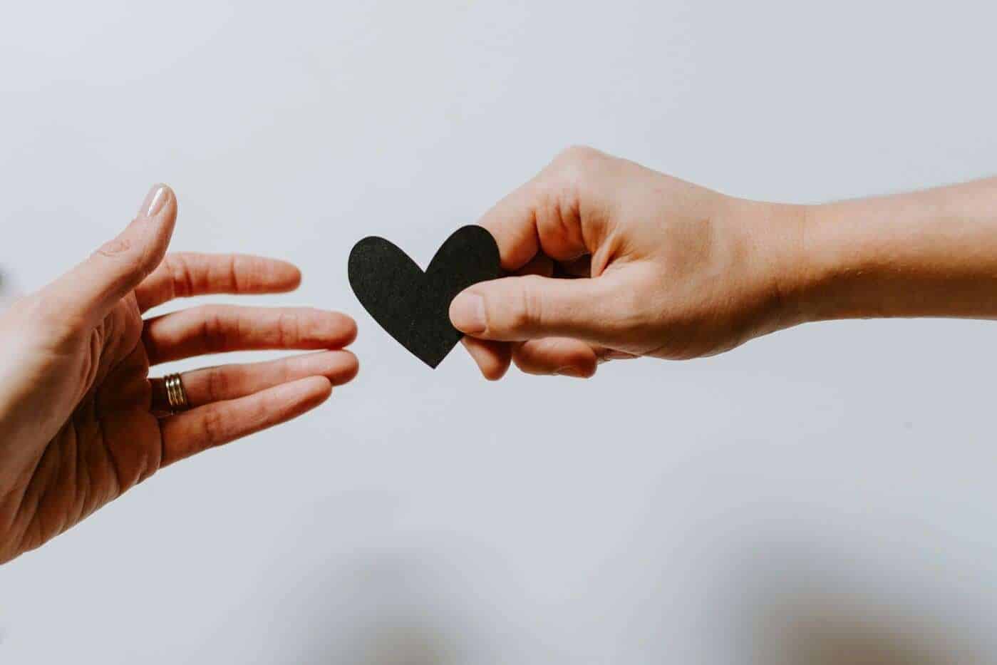Corazón de papel negro siendo entregado en una mano a otra mano.