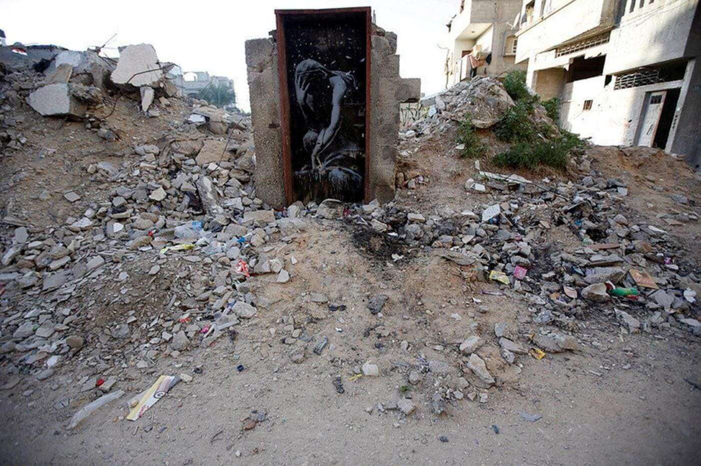 Ruinas de un edificio destruido con graffiti de una mujer en la puerta principal. Ambiente urbano con escombros y basura en las calles.