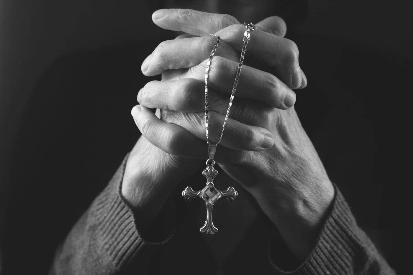 Alt: Manos entrelazadas sosteniendo un collar con un crucifijo en blanco y negro.