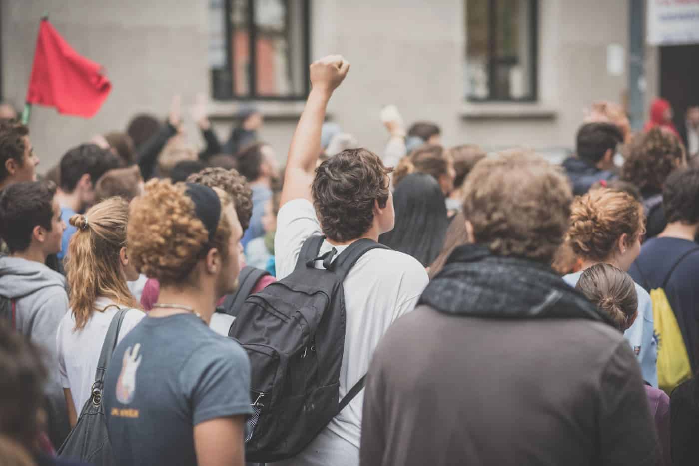 Manifestantes en una protesta urbana con una persona levantando el brazo en señal de protesta.