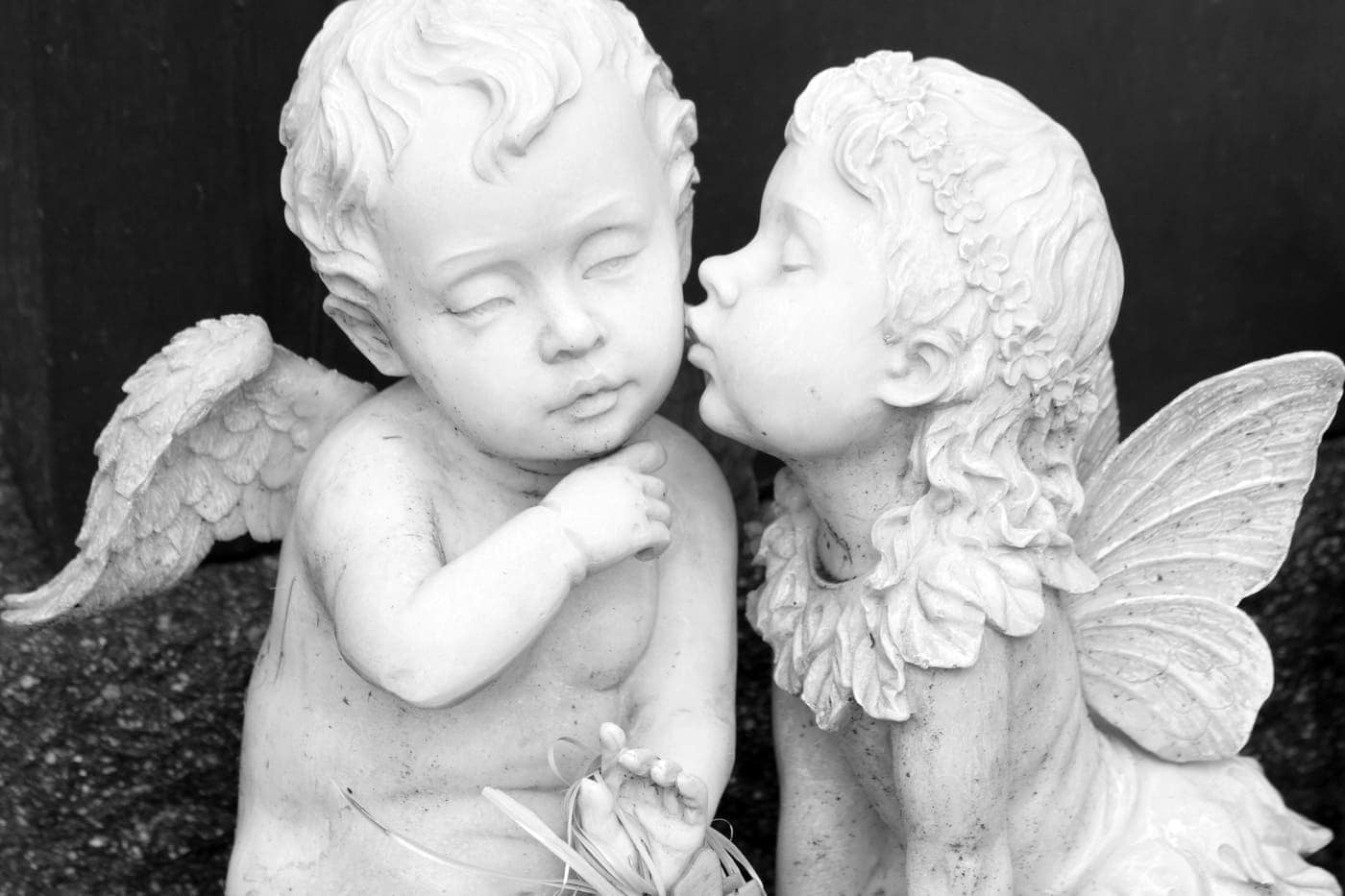 Niño con alas y niña con orejas de mariposa, escultura en tonos blancos y grises mostrando ternura y amistad.