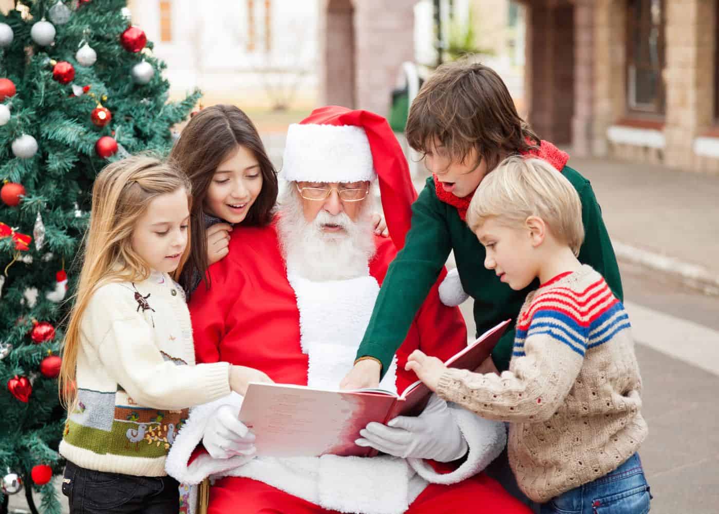 Árbol de Navidad decorado con adornos navideños y niños entregando regalos a Santa Claus en un ambiente festivo.