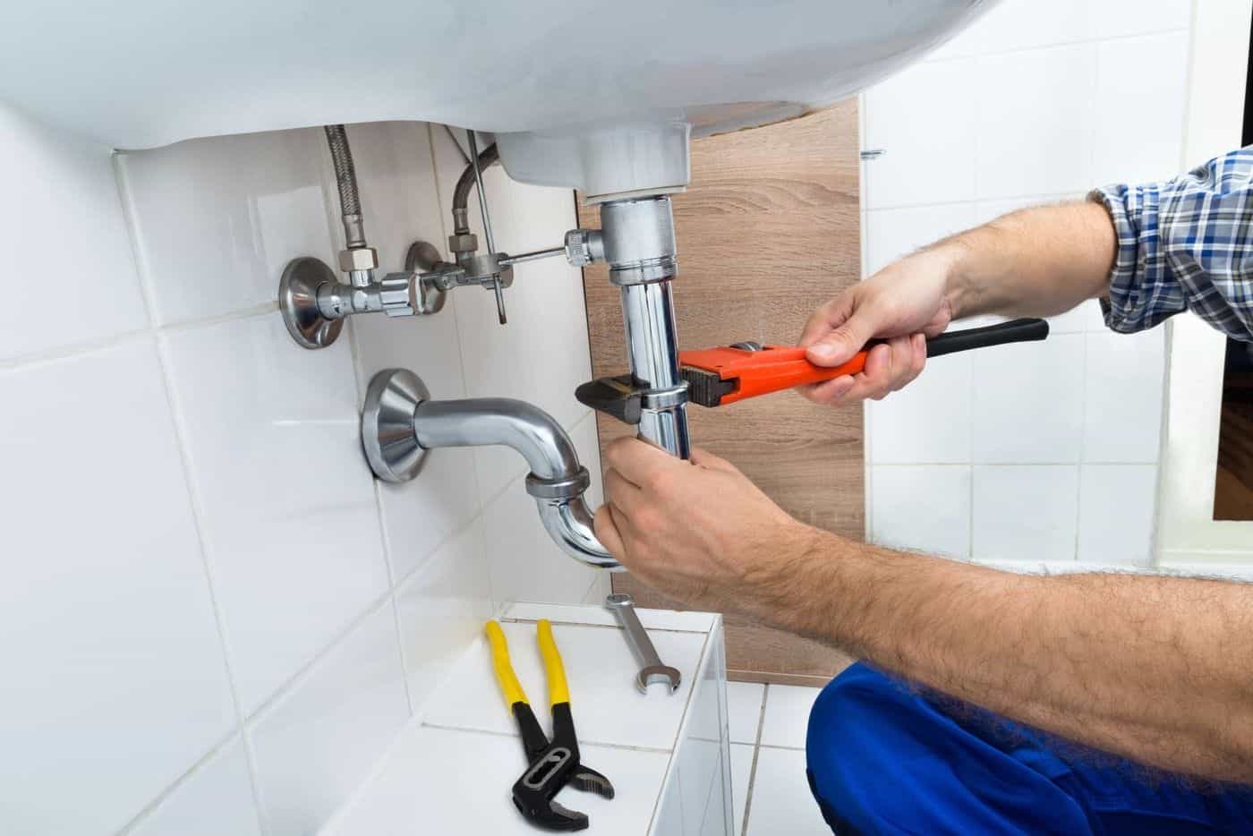 Reparación de tuberías de lavabo, plomero arreglando fuga con llave inglesa en el hogar.