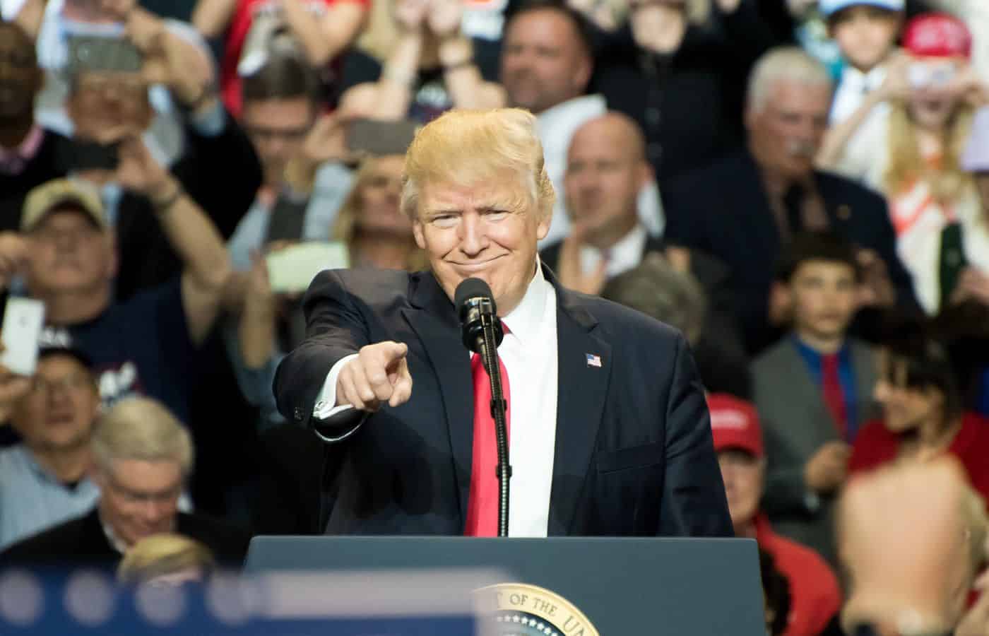 Donald Trump en un mitin político, saludando a la audiencia con gesto confiado.