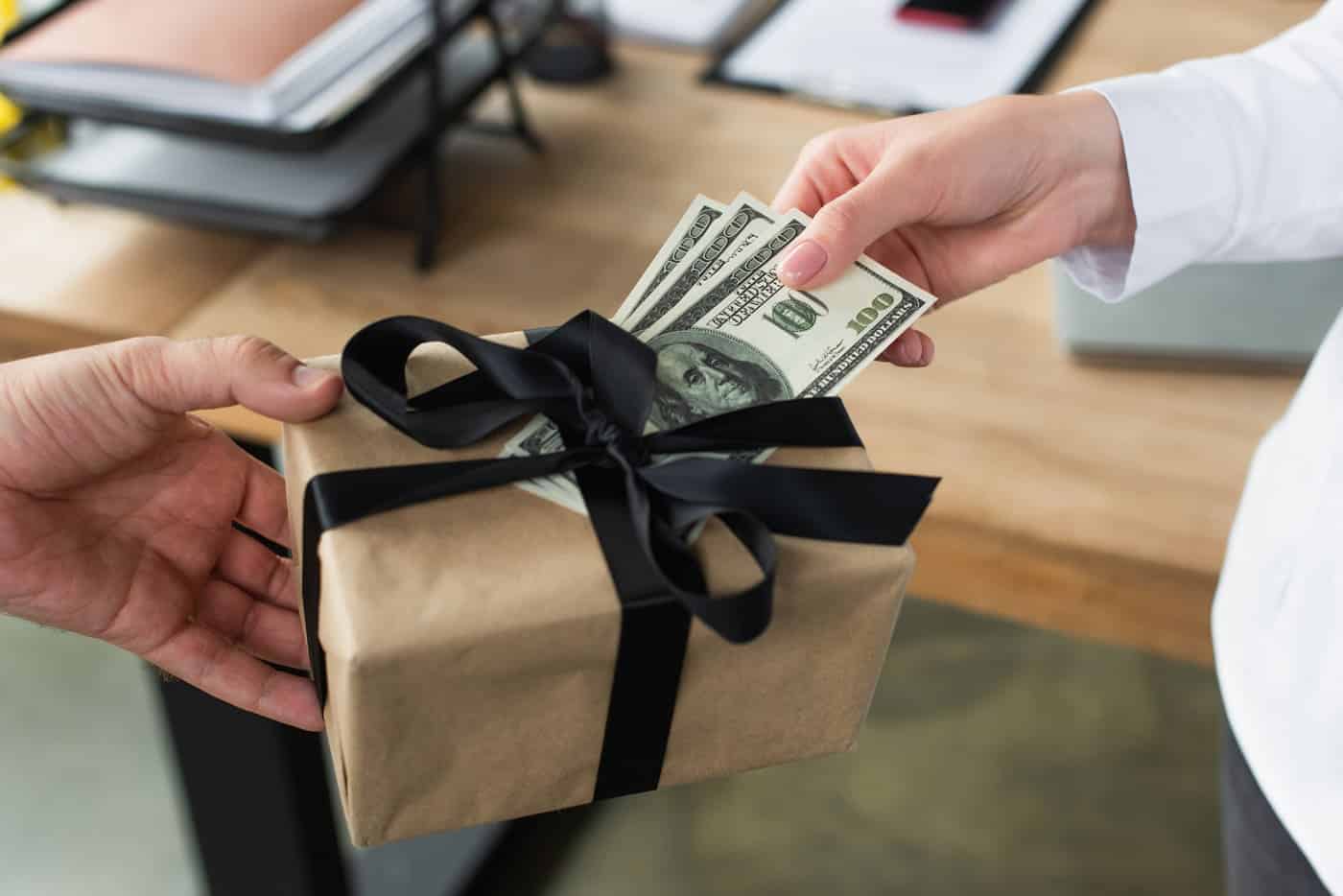 Dinero en efectivo siendo entregado en un regalo envuelto con lazo negro.