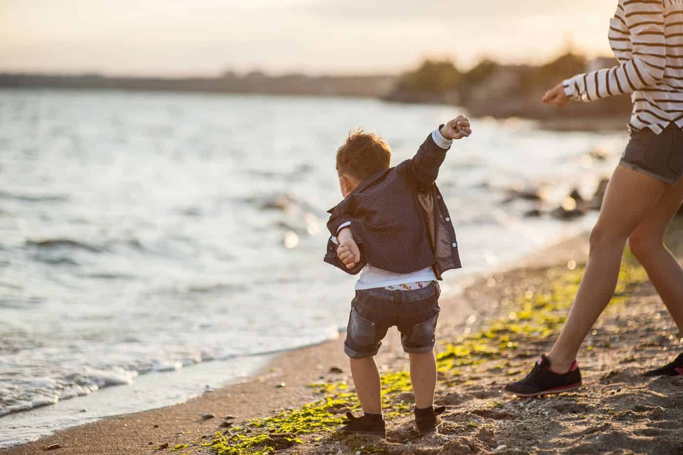 Niño jugando en la playa con un adulto, disfrutando del atardecer junto al mar.