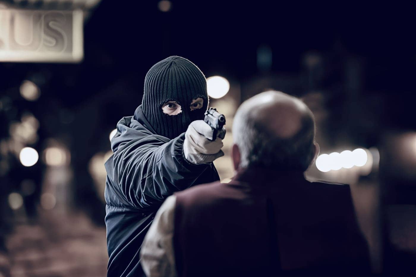 Amenaza de violencia con un hombre con máscara y pistola en mano, enfrentando a un adulto mayor en un ambiente nocturno.
