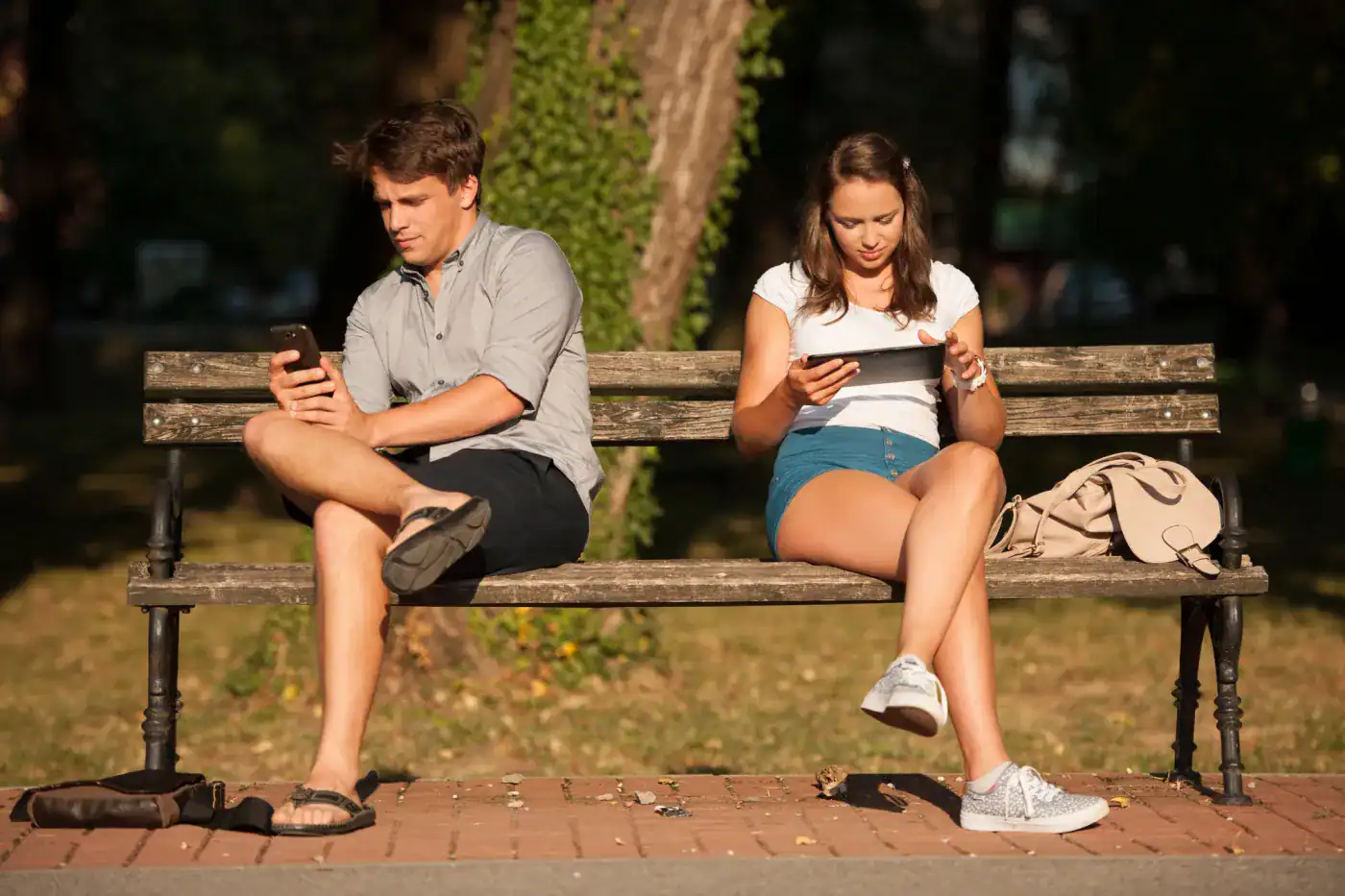 Jovenes usando teléfonos en un banco del parque.
