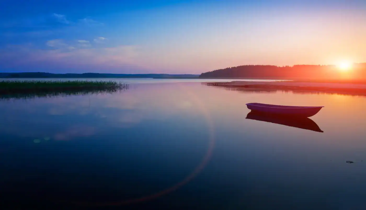 Barco en un lago al atardecer con reflejo en el agua y cielo colorido, asociado a filosofía y tranquilidad.