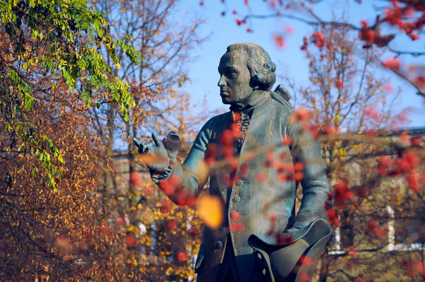 A statue of a man in a suit is surrounded by autumn leaves.