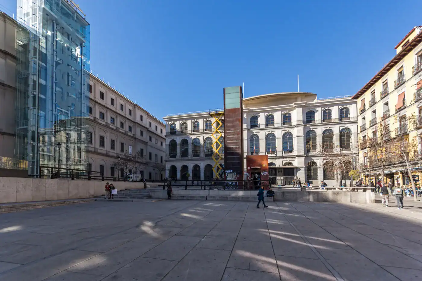 Moderno edificio en una plaza urbana con estructuras de vidrio y arquitectura clásica.