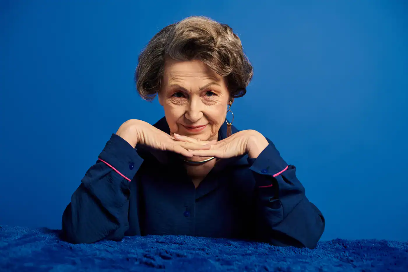 Pensadora mayor sonriendo, con fondo azul, representando filosofía y sabiduría.