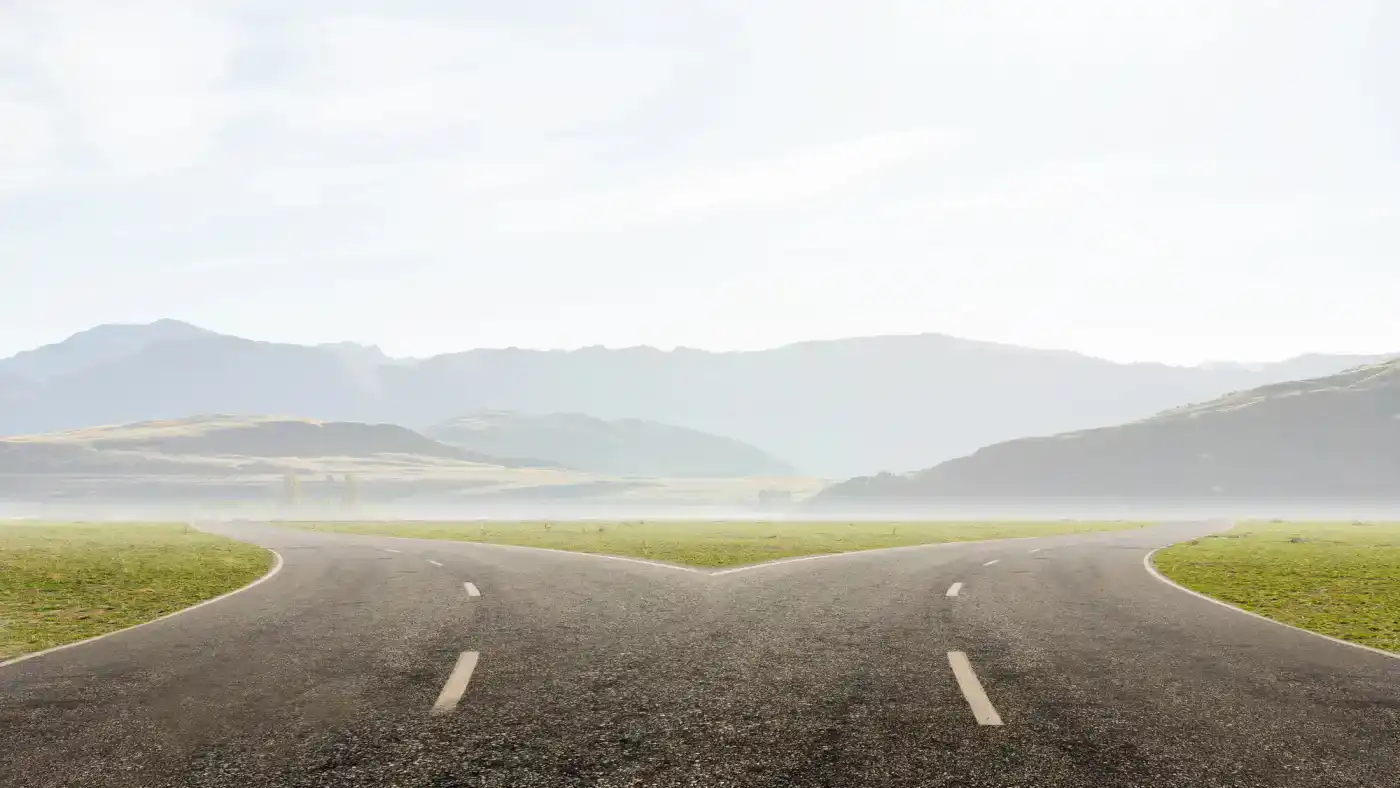 Camino en bifurcación con paisaje montañoso y cielo despejado, simbolizando decisiones filosóficas y caminos de pensamiento.