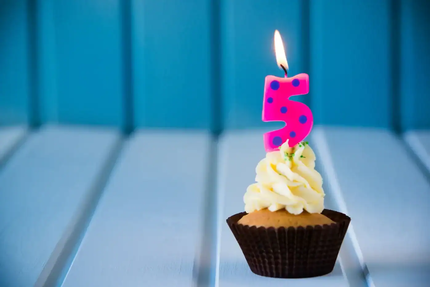 Feliz cumpleaños número 5 con cupcake y vela de número cinco en color rosa con puntos morados.