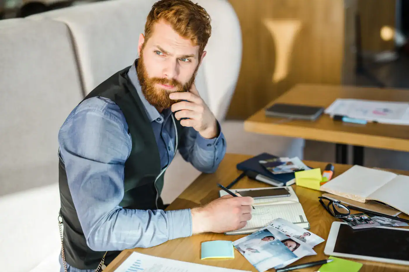 Pensador reflexivo con barba en un entorno de trabajo, mirando pensativo y rodeado de documentos y tecnología.