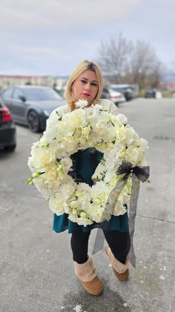 Coroană funerară albă rotundă, realizată din trandafiri și crizanteme naturale, cu panglică neagră elegantă.