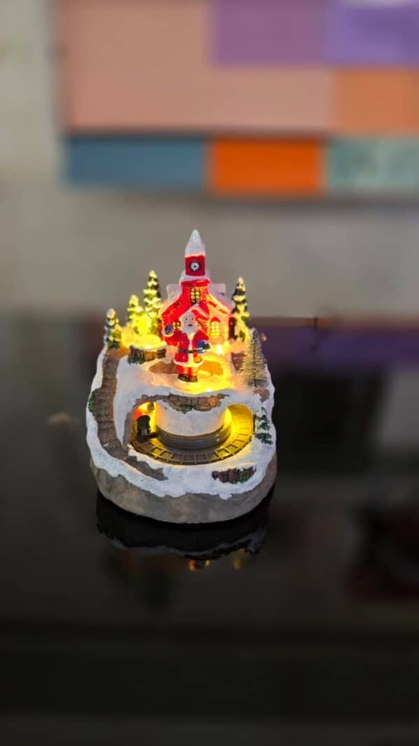 scenă decorativă crăciun cu moș crăciun, biserică iluminată și trenuleț în mișcare