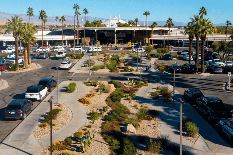 An elevated view of an airport terminal entrance with cars, palm trees, and desert landscaping under a clear sky.
