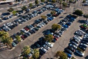 Aerial view of a large, crowded parking lot with hundreds of cars, SUVs, and trucks, surrounded by palm trees.