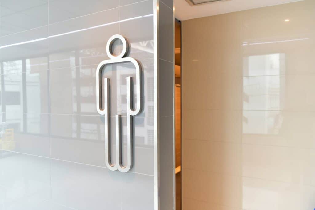 A silver male restroom symbol on a glossy light gray tiled wall.