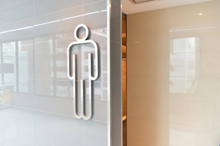 A silver male restroom symbol on a glossy light gray tiled wall.