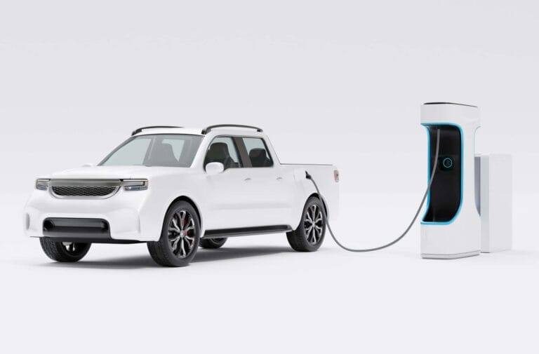 A white electric pickup truck is charging at a white and blue electric vehicle charging station against a white background.