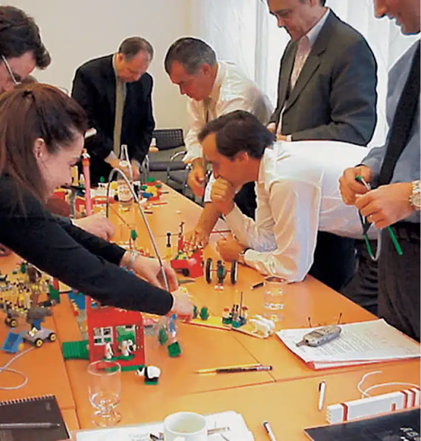 A hand building a duck out of six LEGO bricks, demonstrating the first step of the LEGO SERIOUS PLAY methodology.