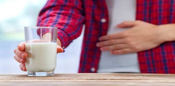 Unopened glass of fresh milk on wooden surface with person in background.
