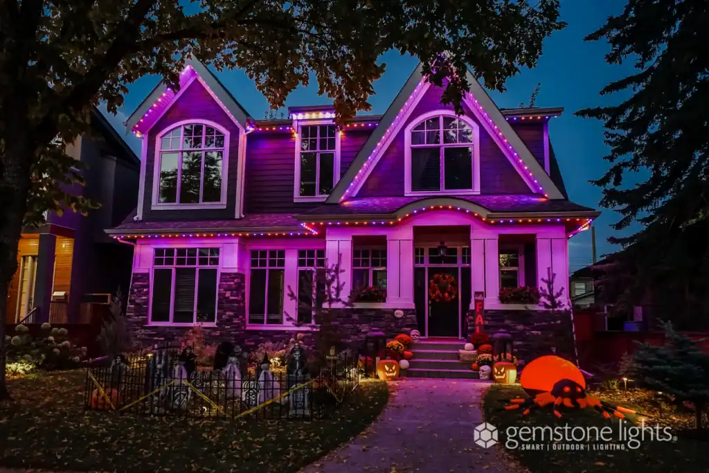A two-story house is decorated with pink and purple lights and Halloween decorations, including pumpkins and an inflatable jack-o’-lantern, at dusk, perfectly capturing the festive spirit that defines what we’re all about us.