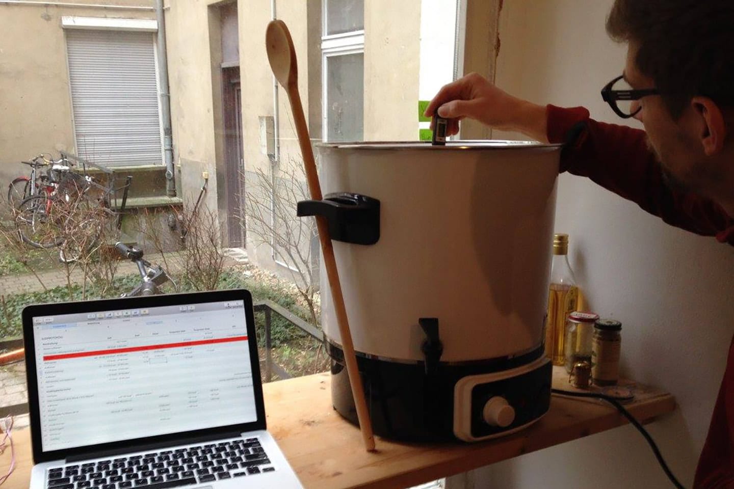 Gärprozess in einer Brauerei, der einen Mann zeigt, der in der FUERST WIACEK Brauerei einen Gärtank überwacht, während ein Laptop Brauereidaten aufzeichnet, mit Schwerpunkt auf handwerklicher Bierproduktion.