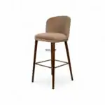 Elegant beige upholstered bar stool with wooden legs and gold footrest for modern kitchen or bar décor.