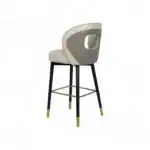 Luxurious beige and gray upholstered bar stool with quilted backrest and gold-accented black wooden legs.