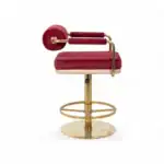 Red velvet upholstered vintage barber chair with gold metal accents for modern salon decor.