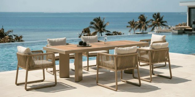 Modern outdoor dining furniture set with wooden table and cushioned chairs overlooking ocean view.
