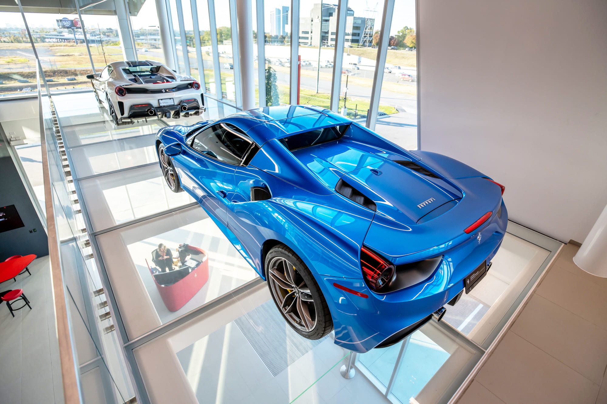 Two luxury cars parked on a structural glass floor panel in a showroom