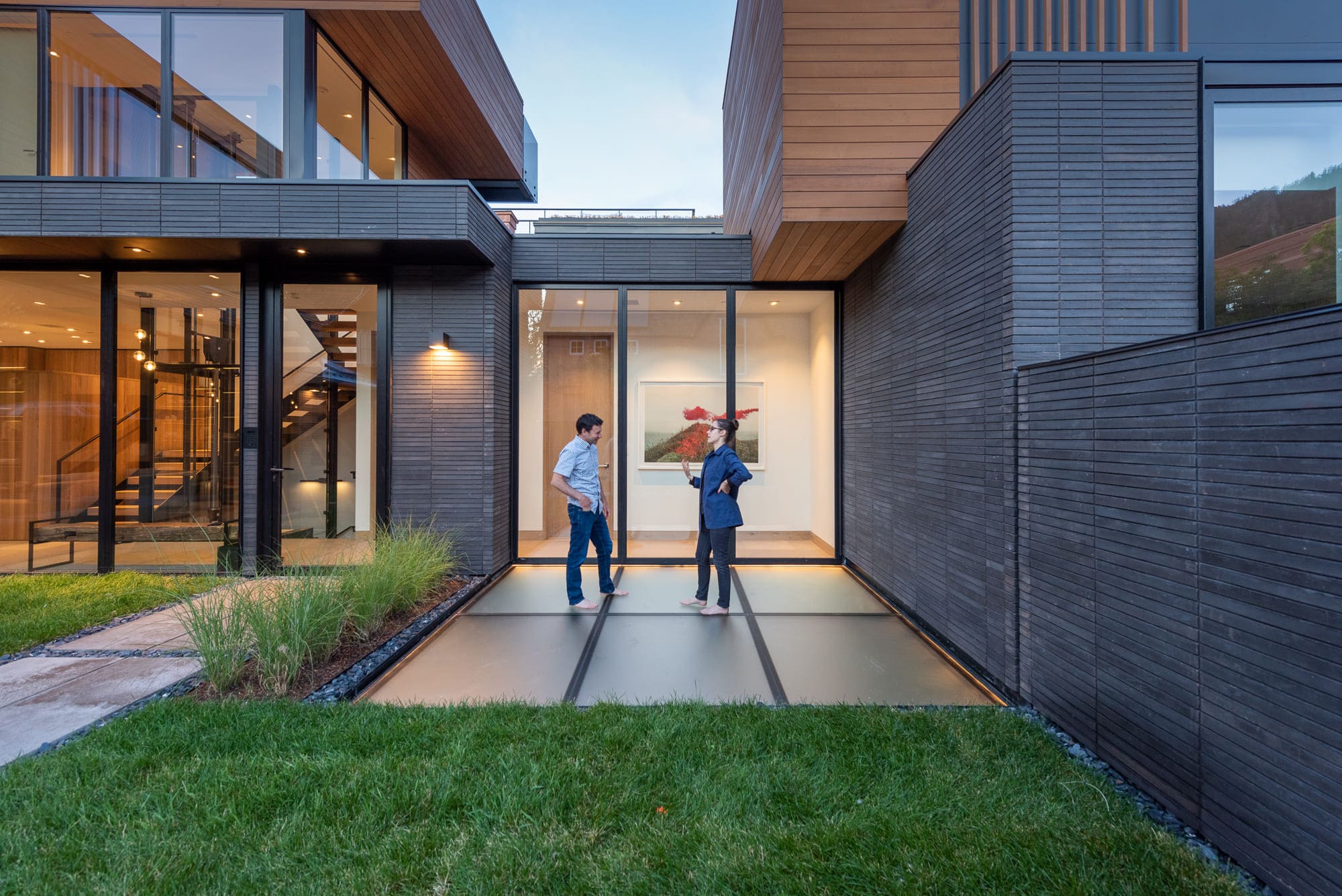 Two people standing on an exterior walkable glass deck at a modern home with floor-to-ceiling windows
