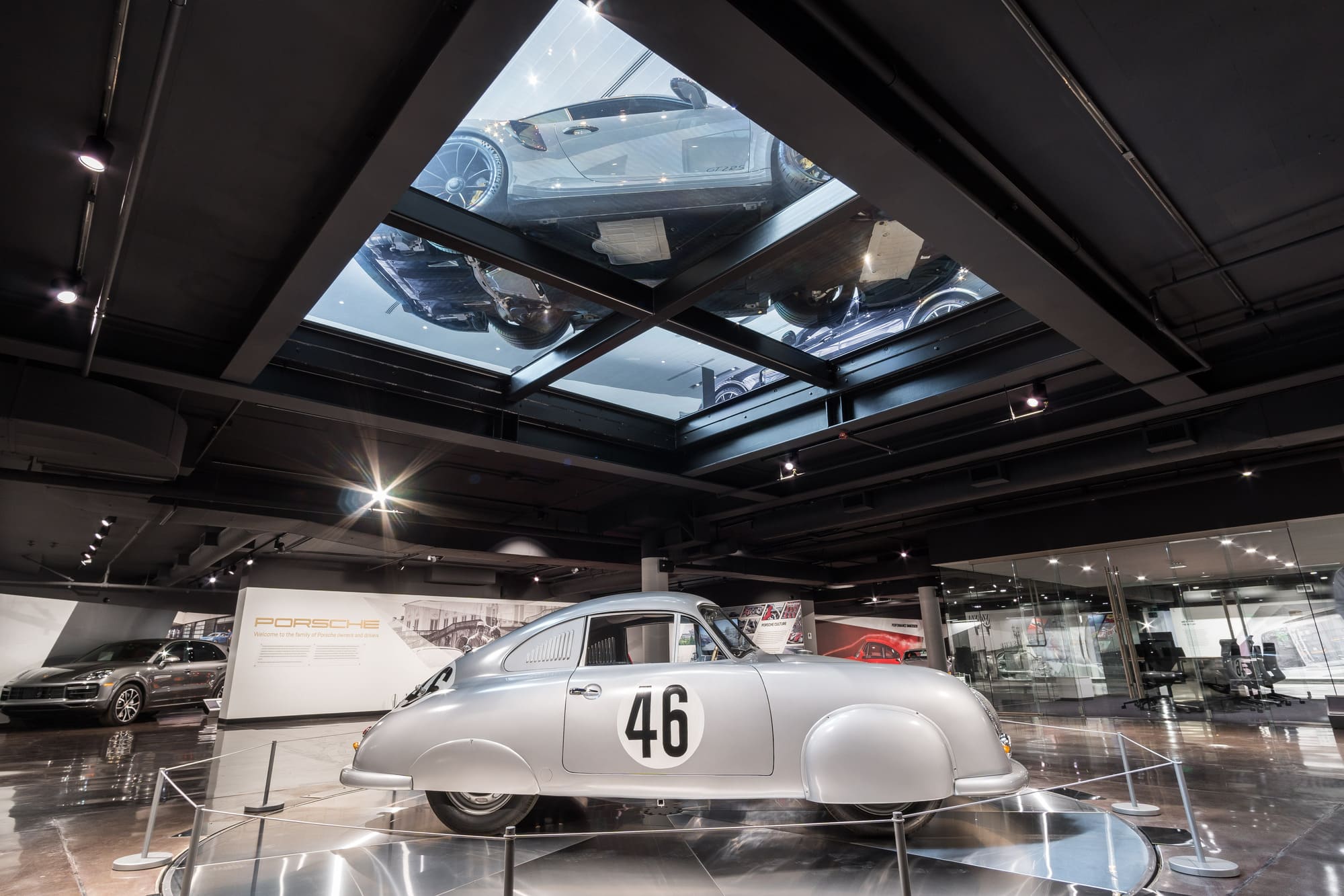 Silver Porsche 356 displayed on a walkable glass floor in a luxury car showroom