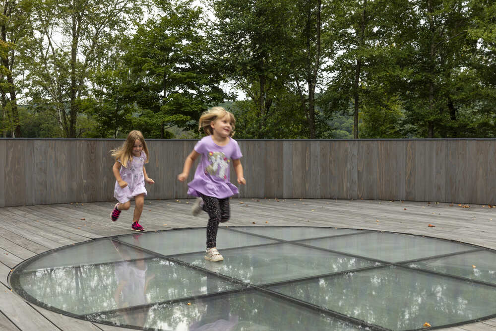 Two children running across a walkable glass floor panel with anti-slip texture