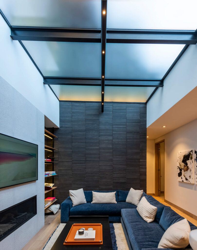 Below-grade living room with a blue sectional lit from above by a SkyFloor Series 1000 walkable skylight