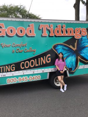 A person stands in front of a truck with "Good Tidings Heating Cooling" and a large blue butterfly graphic on its side.