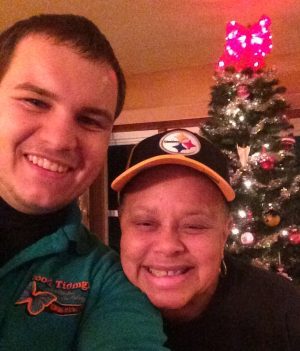 Two people smiling in front of a decorated Christmas tree, one wearing a Pittsburgh Steelers cap.