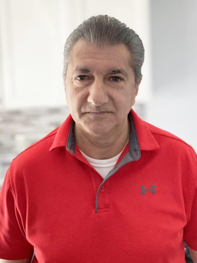 Middle-aged man with gray hair wearing a red Under Armour polo shirt stands indoors in a well-lit room with a neutral expression.