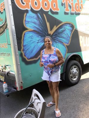 Smiling woman in a sleeveless top and shorts stands in front of a truck with a large blue butterfly graphic on the side.