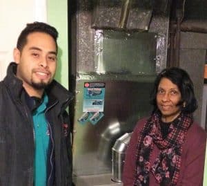 A man and a woman stand indoors near a large metal HVAC unit, looking at the camera.