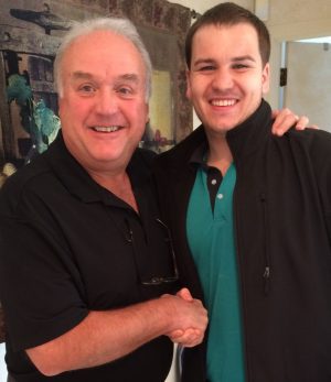 Two men smiling and shaking hands while posing for a photo indoors.