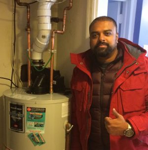 A person in a red jacket stands next to a water heater, giving a thumbs-up gesture.