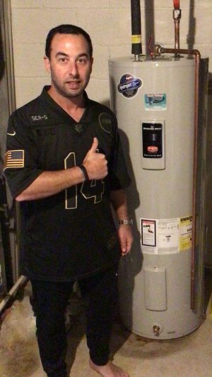 A man standing indoors gives a thumbs up next to a water heater.